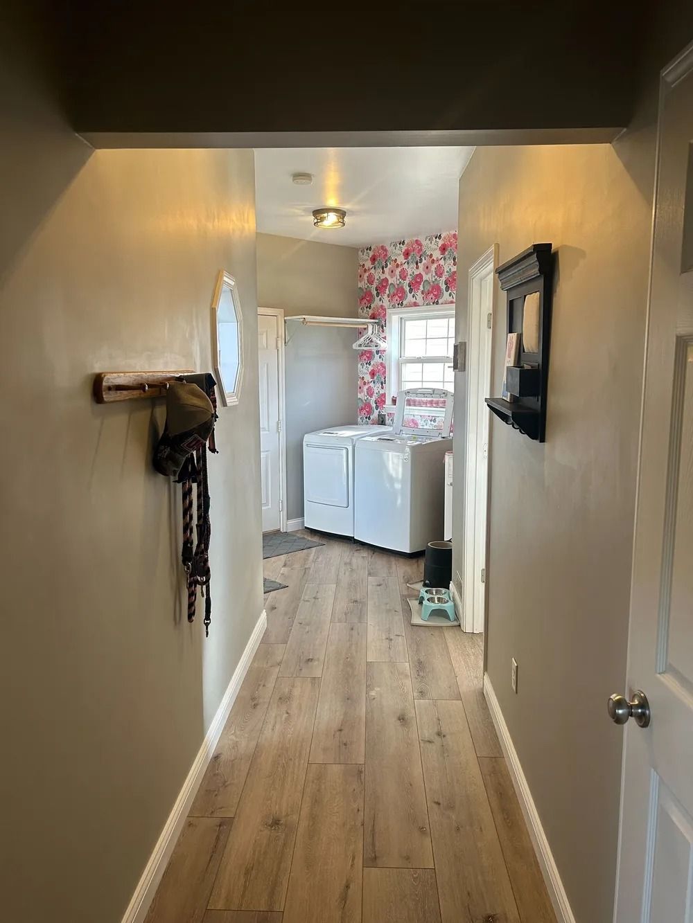 Narrow hallway with wood floors leading to a laundry room with a washer, dryer, and floral wallpaper.