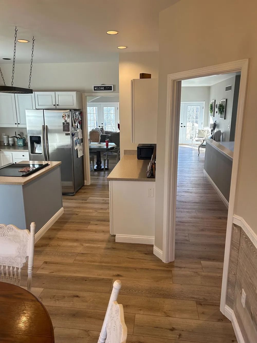 Modern kitchen and hallway with stainless steel appliances, white cabinets, and wood-look flooring.