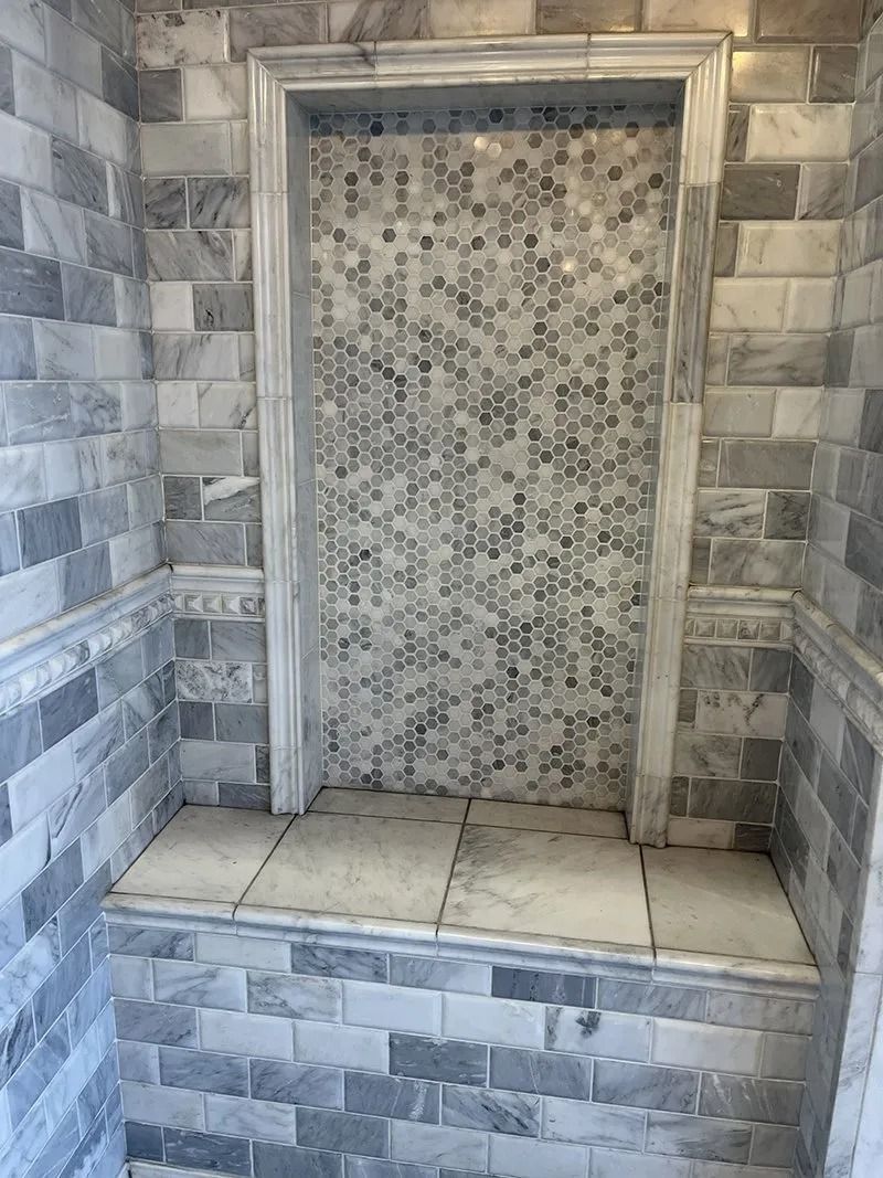 Built-in tiled shower niche with gray stone surround and mosaic back panel