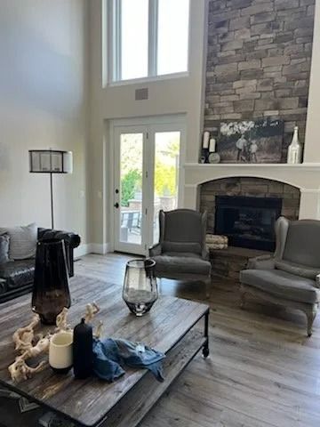Bright living room with tall windows, stone fireplace, gray chairs, and a wooden coffee table