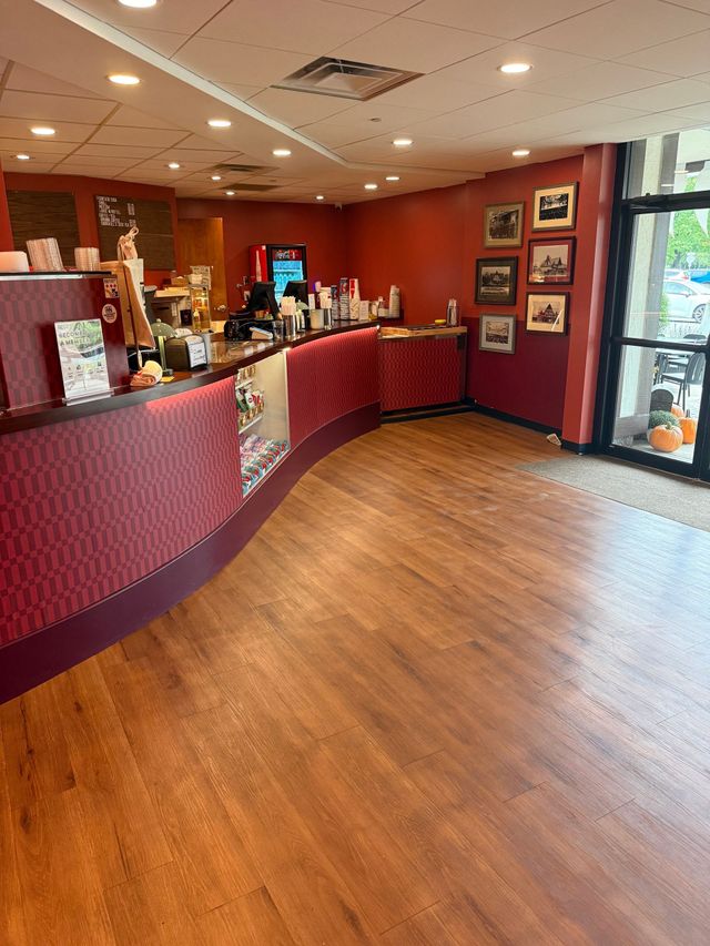 Empty restaurant lobby with red curved counter, wood floor, and framed photos on the wall.