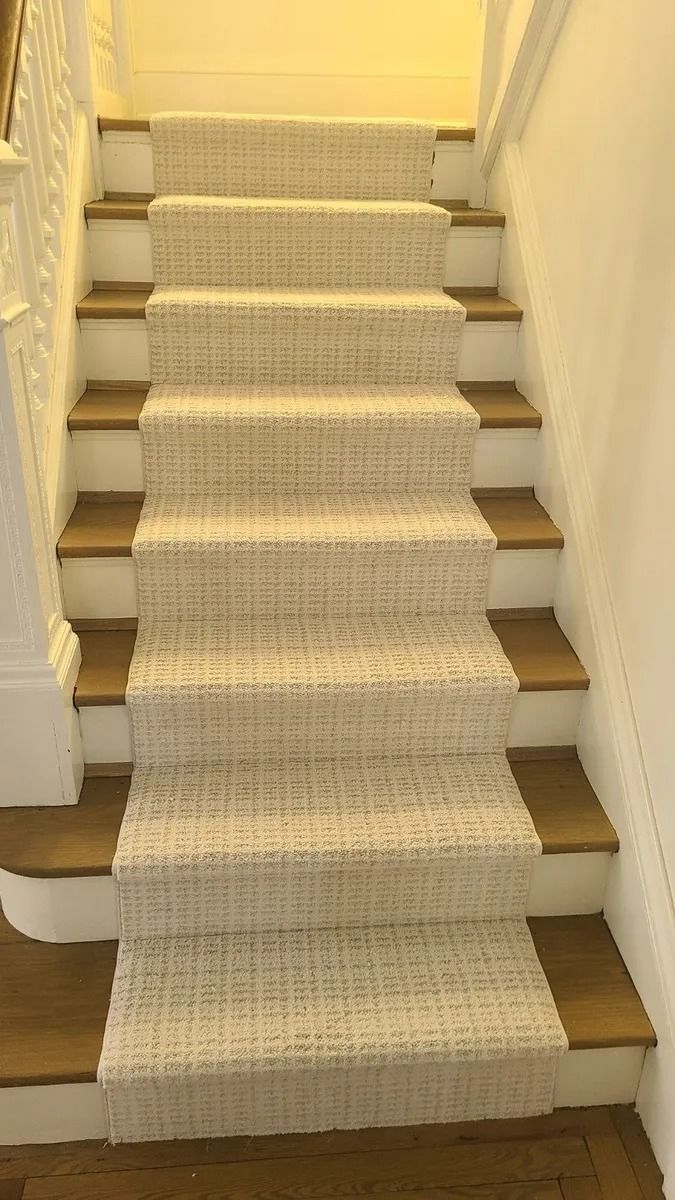 Carpeted staircase with white walls and tan carpet runner, viewed from the bottom upward.