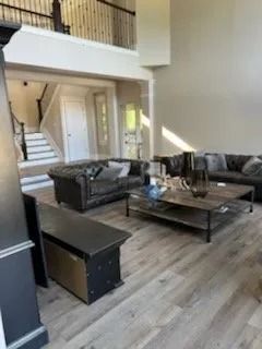 Spacious modern living room with black leather sofas, coffee table, staircase, and loft balcony.