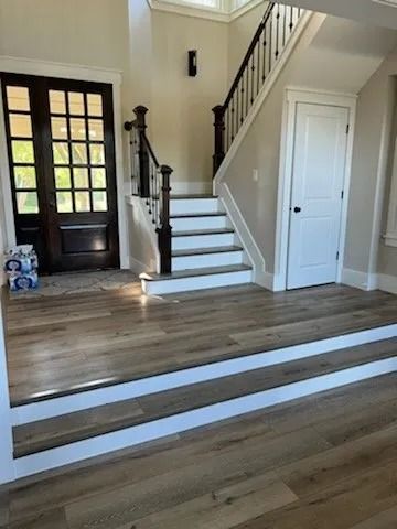 Entryway with wood floors, stairs, and two long white floor tracks across the room.