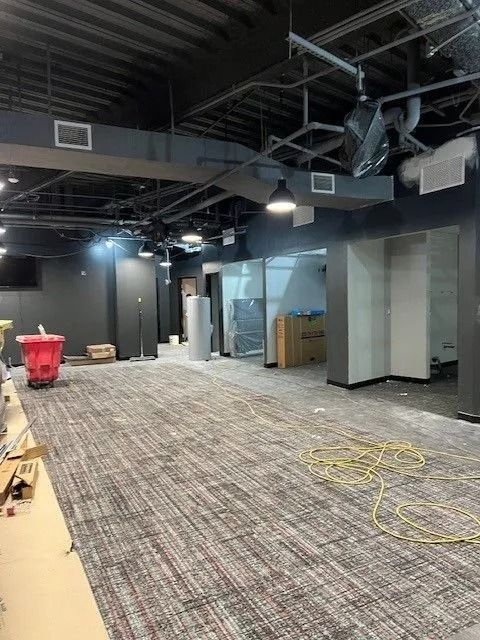 Empty office interior with exposed ceiling, carpet tiles, and scattered cables during renovation