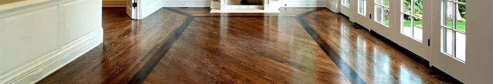 Empty sunlit room with polished dark wood floors and windows along one side