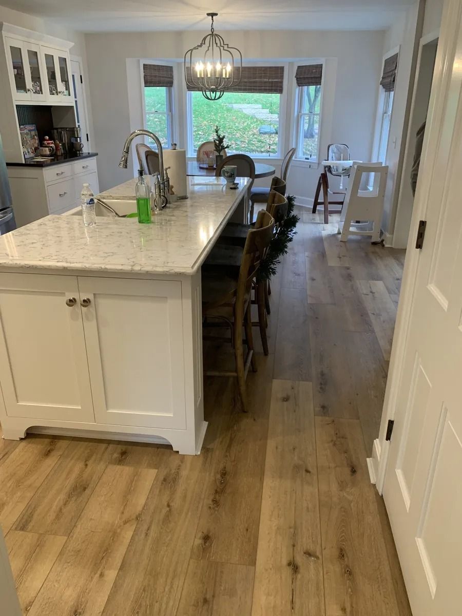 Bright kitchen with white island, wood floors, barstools, and dining area by large windows