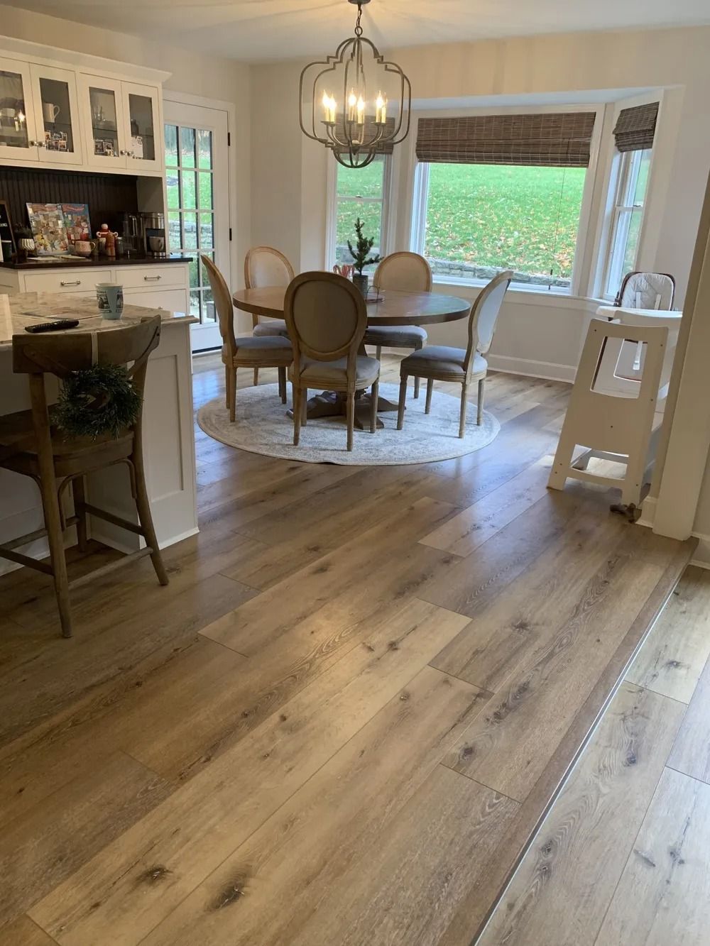 Bright kitchen-dining room with hardwood floors, round table, chairs, bay window, and hanging pendant light