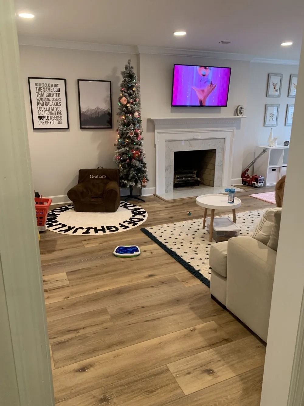Cozy living room with fireplace, TV, Christmas tree, and beige sofa, with a cat bed on the floor.