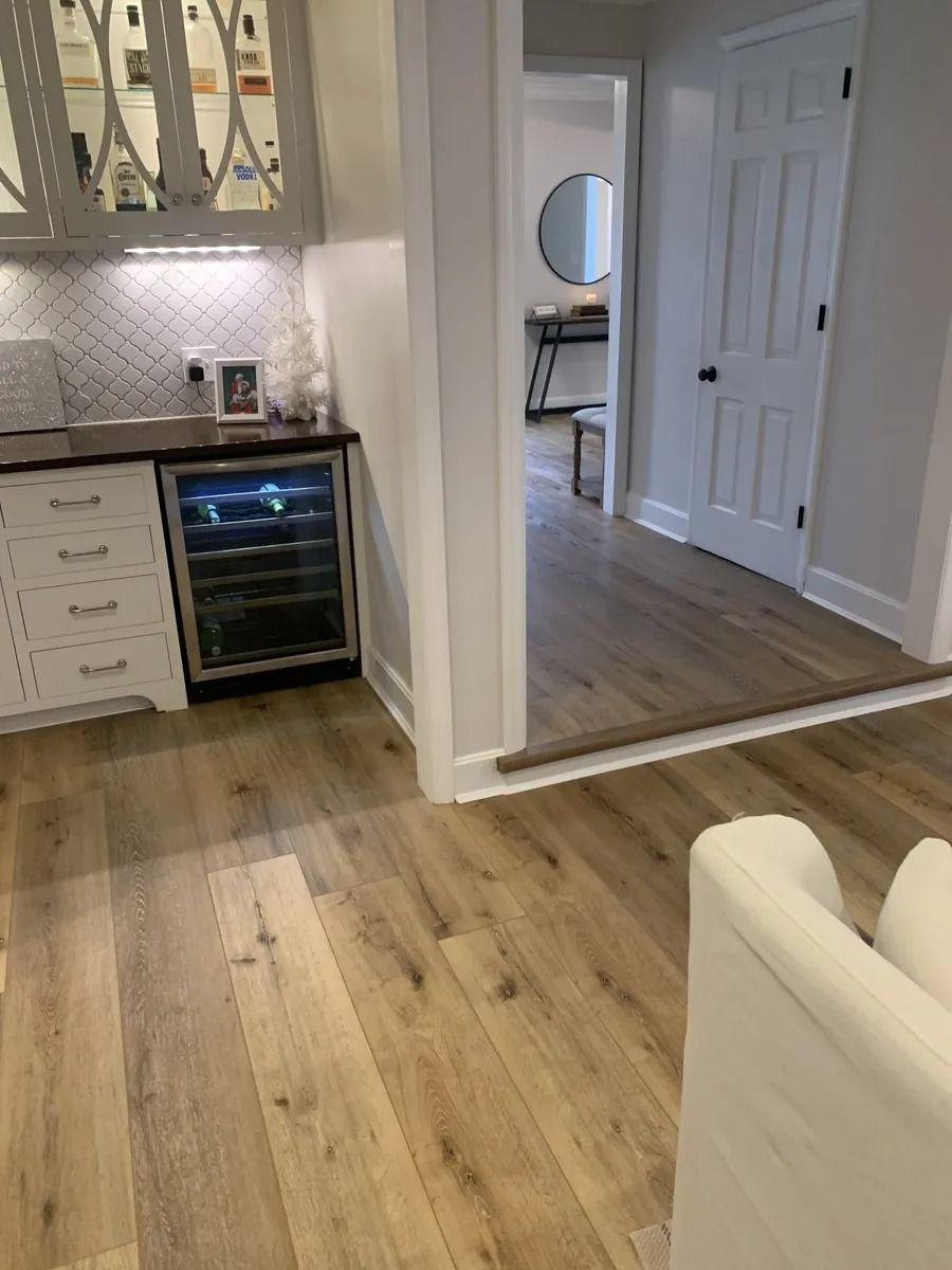 Bright kitchen with wood floors, white cabinets, wine fridge, and hallway view into another room