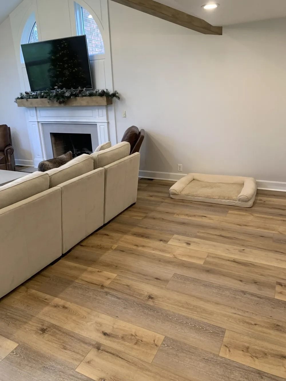Living room with fireplace, mounted TV, beige sofa, and a dog bed on wood flooring