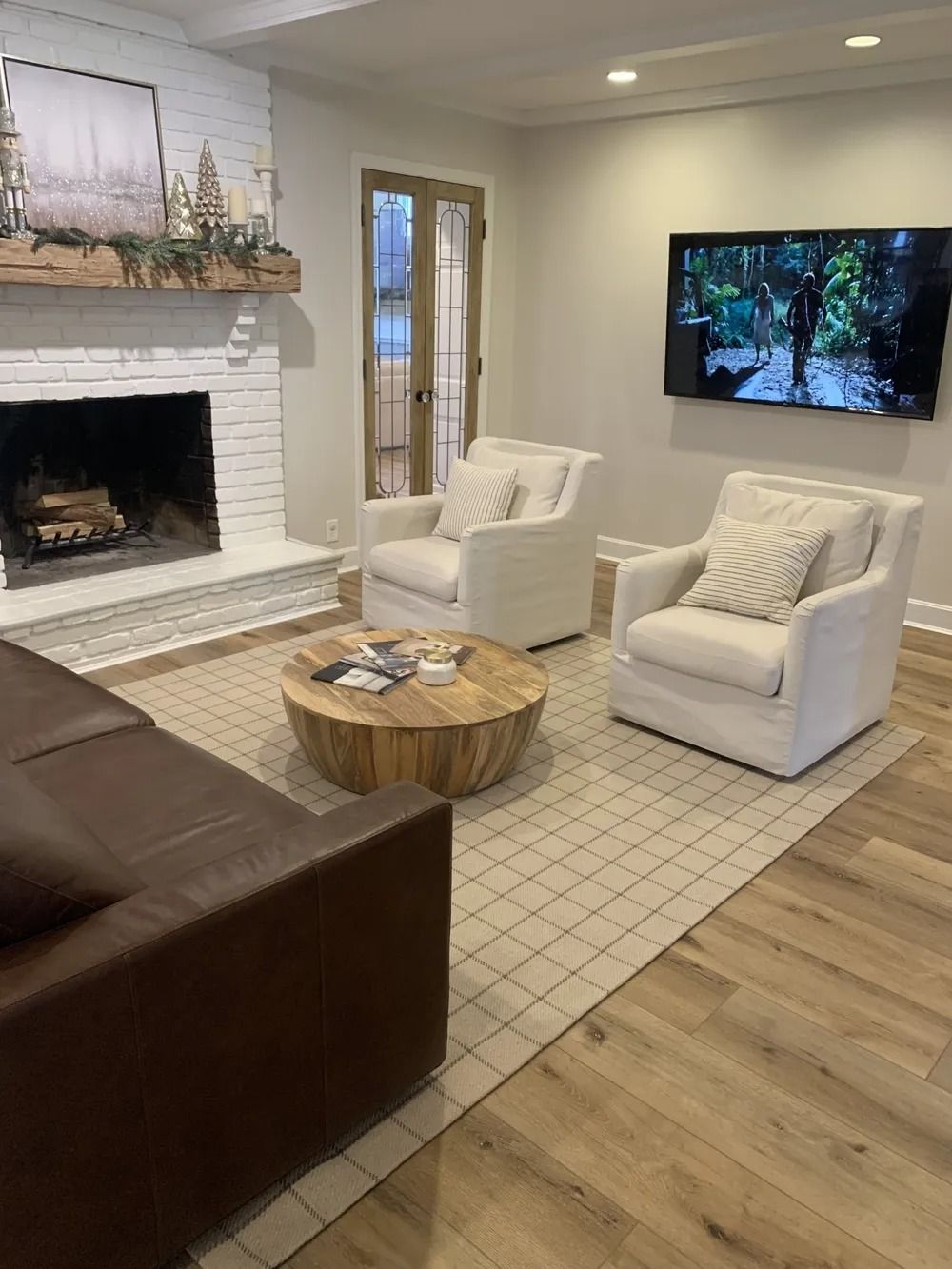 Modern living room with fireplace, white chairs, round coffee table, wall TV, and hardwood floors