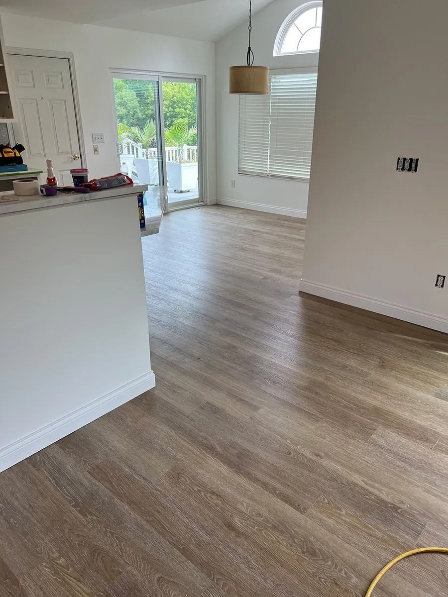 Empty bright room with wood flooring, kitchen counter, and sliding glass door to a patio.
