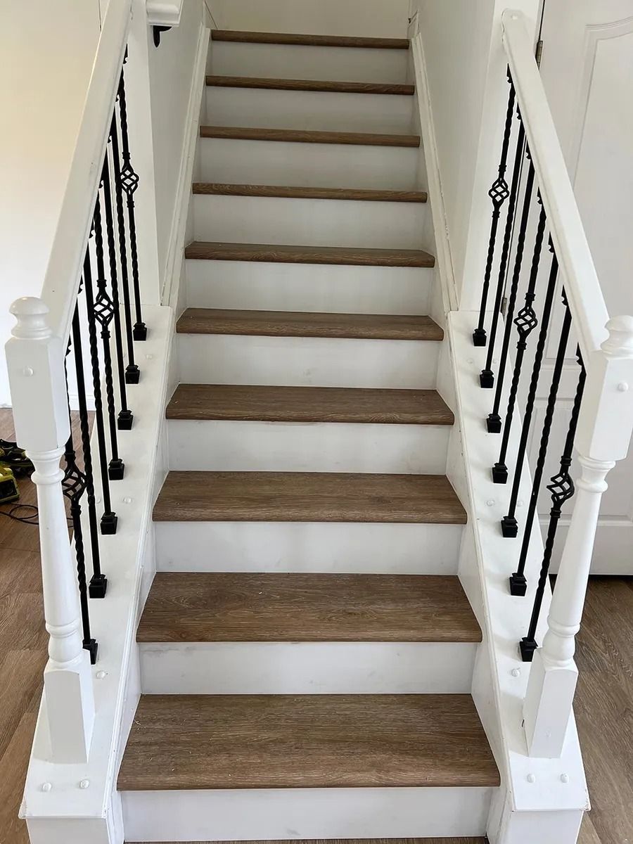 Interior staircase with white railings, black balusters, and wood steps in a bright hallway