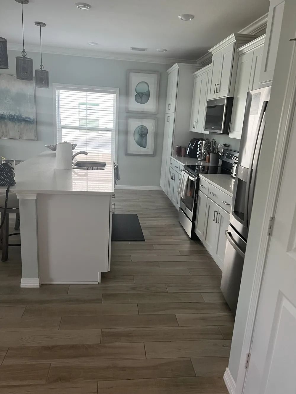 Bright modern kitchen with white cabinets, island, stainless appliances, and wood-look flooring.