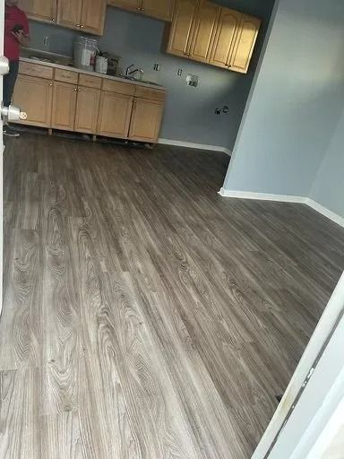 Empty room with wood-look flooring and a small kitchen area with light wood cabinets