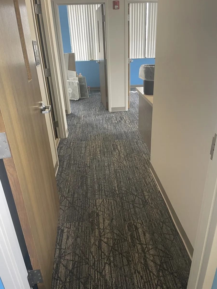 Hallway in an office with carpet, doors, and blue chairs visible ahead