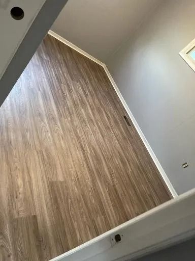 Empty room with wood-look flooring, light gray walls, and a small window.