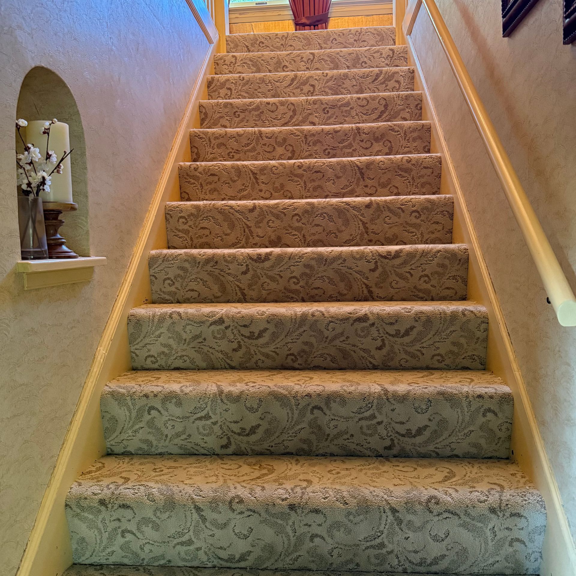 Carpeted indoor staircase with tan walls and wooden handrails, leading upward