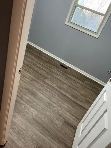 Open white door to a gray room with wood-look flooring and a small window.