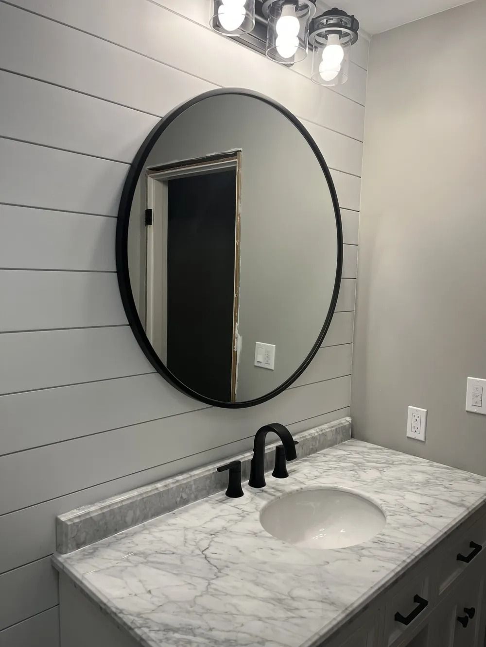 Modern bathroom vanity with round mirror, marble countertop, black faucet, and wall-mounted lights