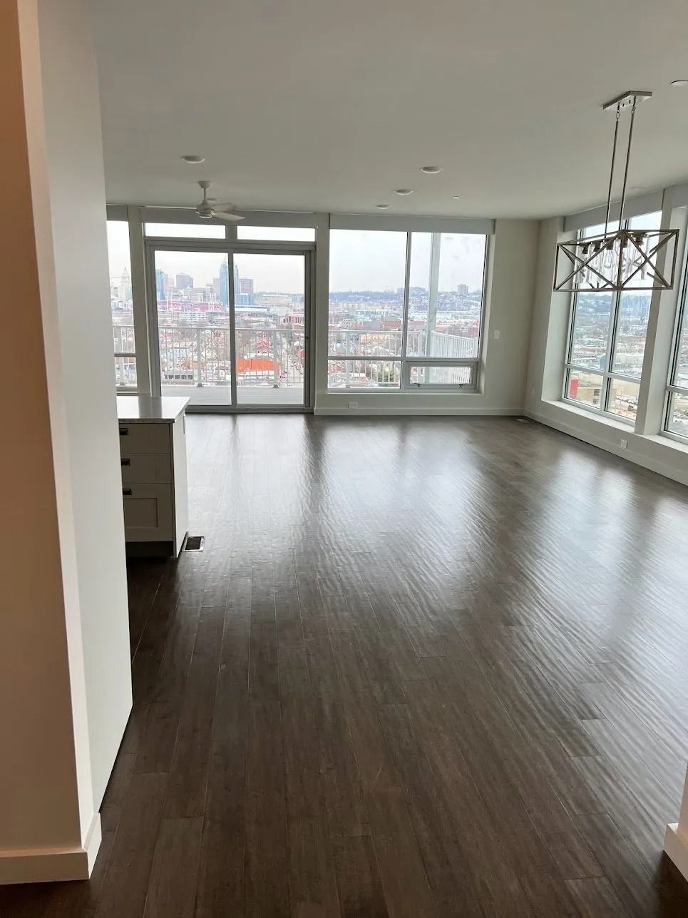 Empty modern apartment living room with dark wood floors and large windows overlooking the city