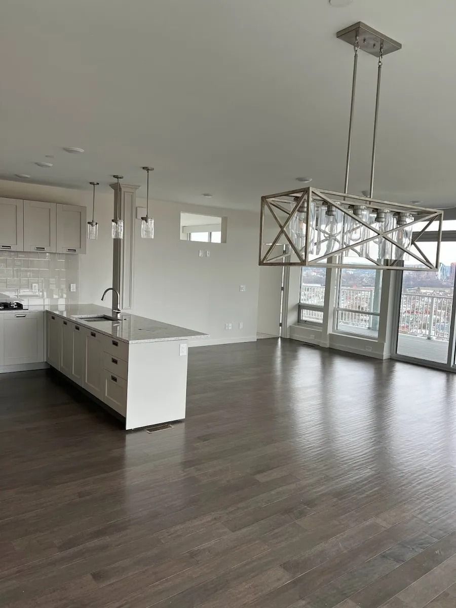 Empty modern kitchen and living area with white cabinets, dark wood floors, and pendant lights