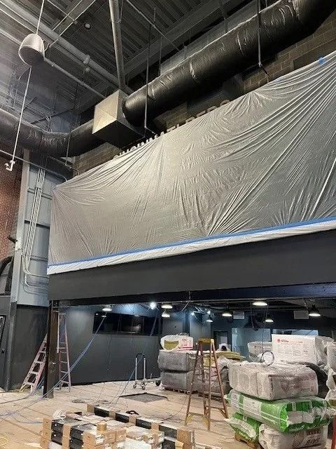Interior renovation site with tall black ceiling, gray tarp wall, ladders, and stacked construction materials