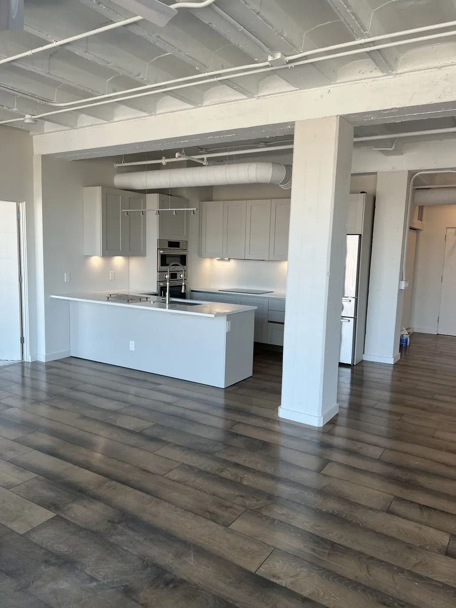 Bright modern kitchen with white cabinets, island, and dark wood floors in an open loft-style space