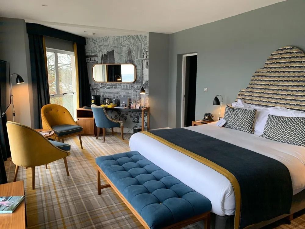 Stylish hotel room with bed, yellow chairs, desk, and large window