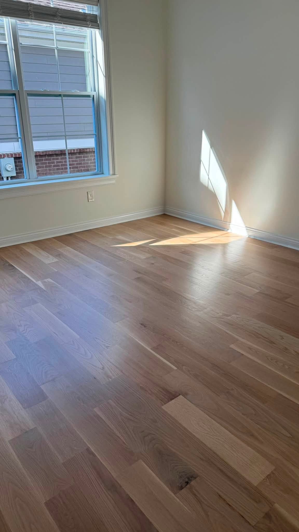 Empty sunlit room with hardwood floors and a window