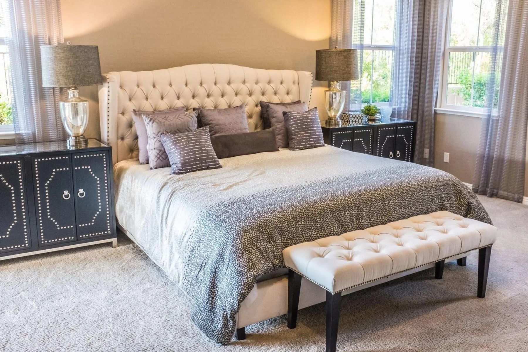 Elegant bedroom with tufted beige bed, gray bedding, mirrored nightstands, and a tufted bench at the foot