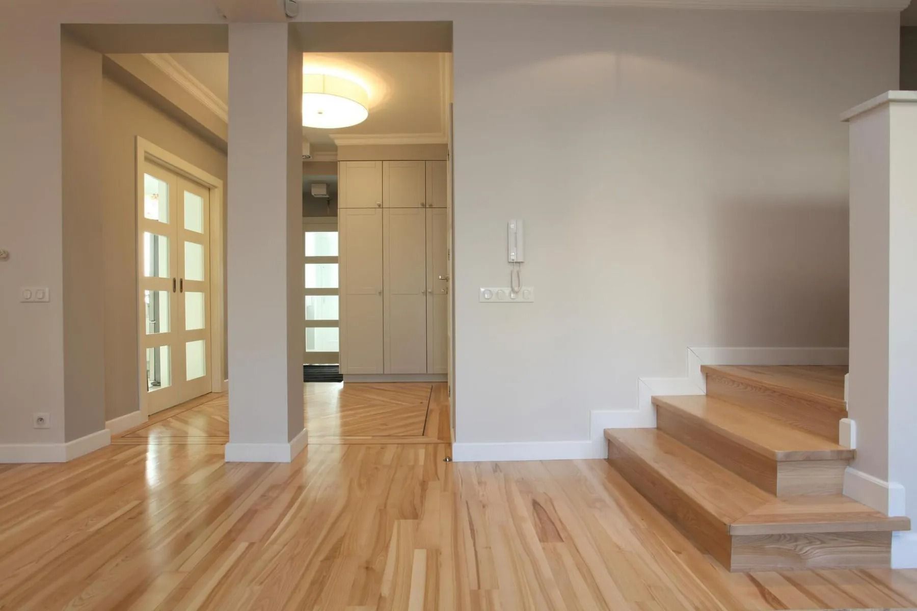 Bright empty hallway with hardwood floors, steps to the right, and a doorway leading to a lit bathroom.