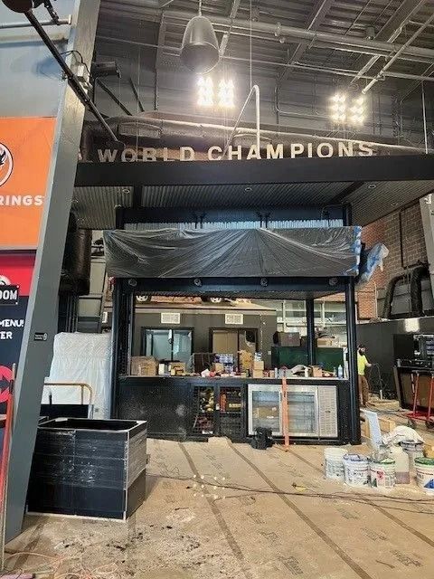 Indoor booth setup under “WORLD CHAMPIONS” sign, with tables, equipment, and supplies in a warehouse-like space