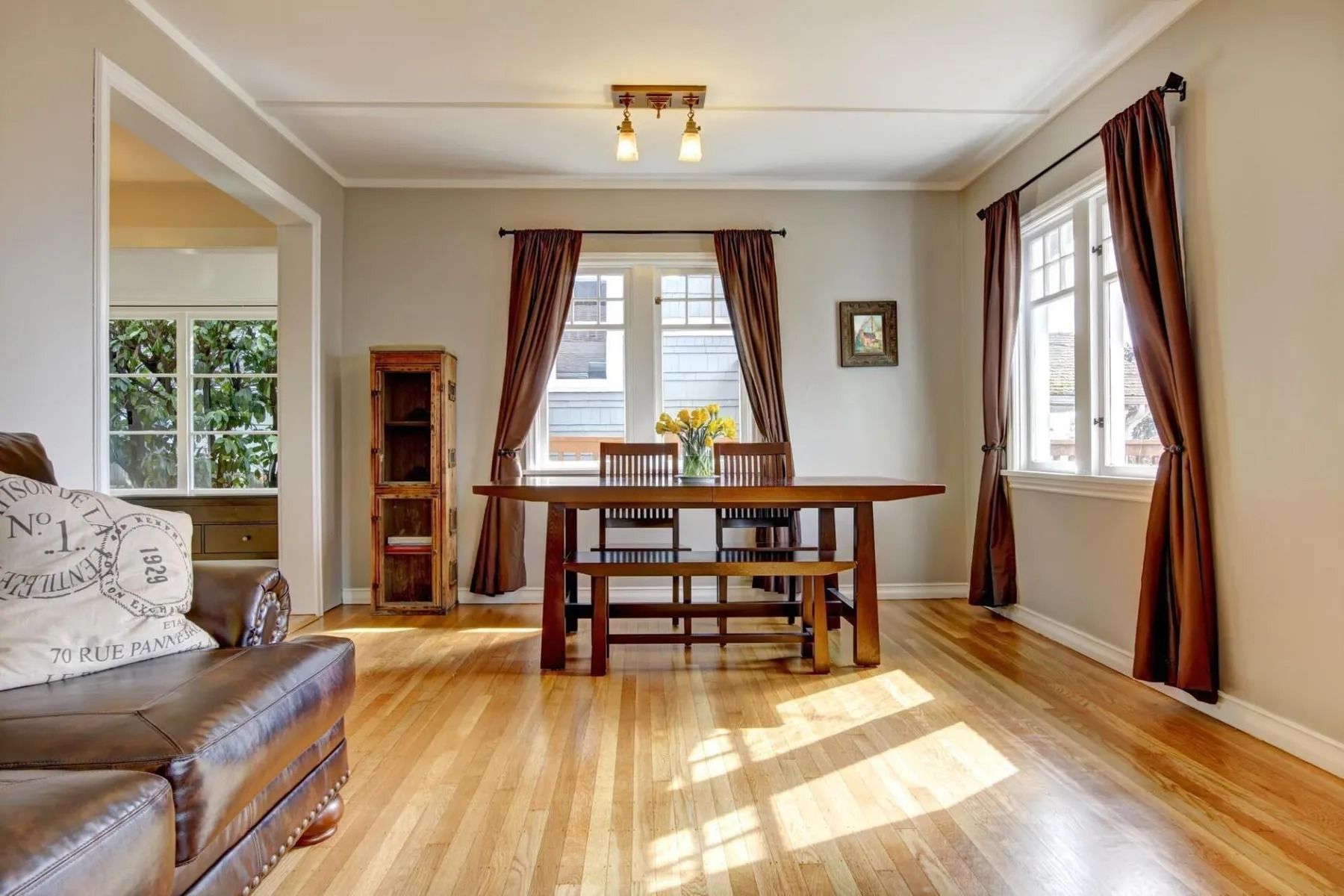 Bright living room with hardwood floors, dining table, sofa, and sunlight through large windows