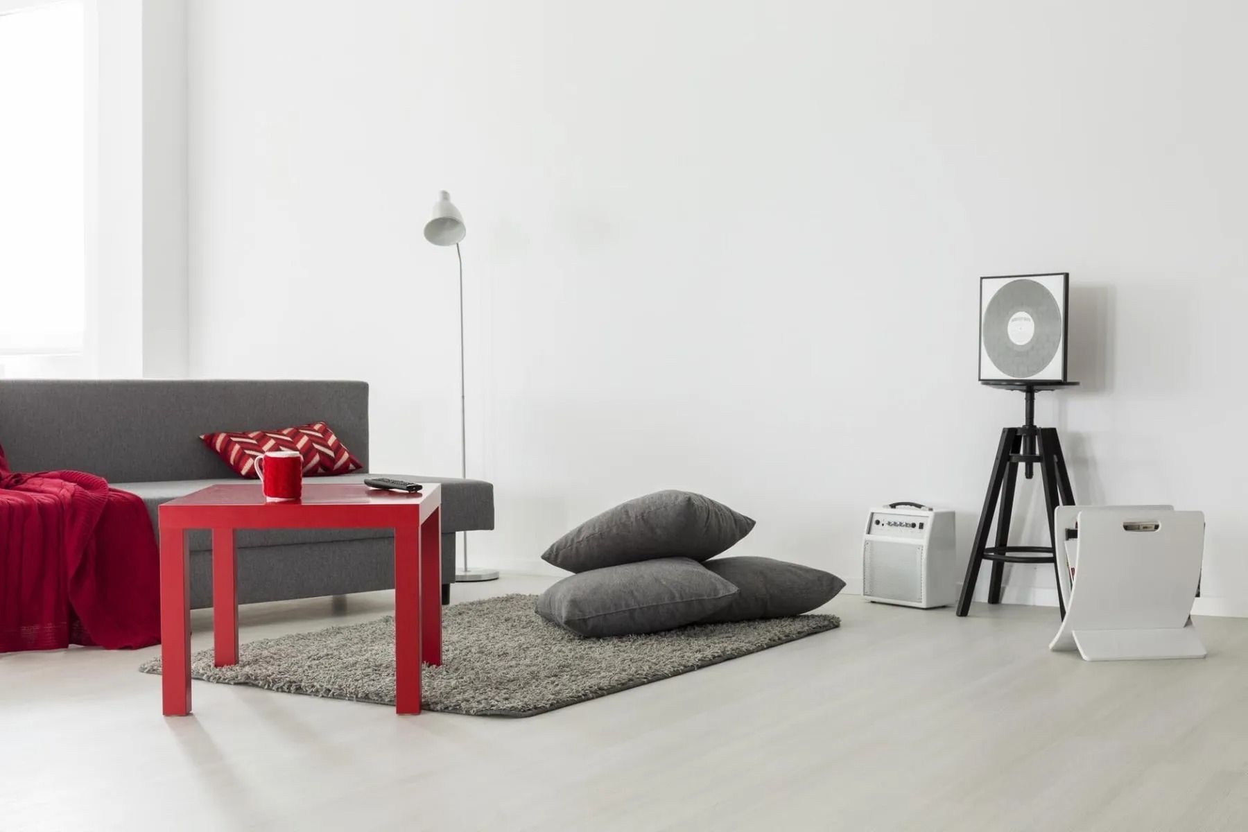 Minimalist living room with red table, gray sofa, beanbags, and a floor lamp on a white background
