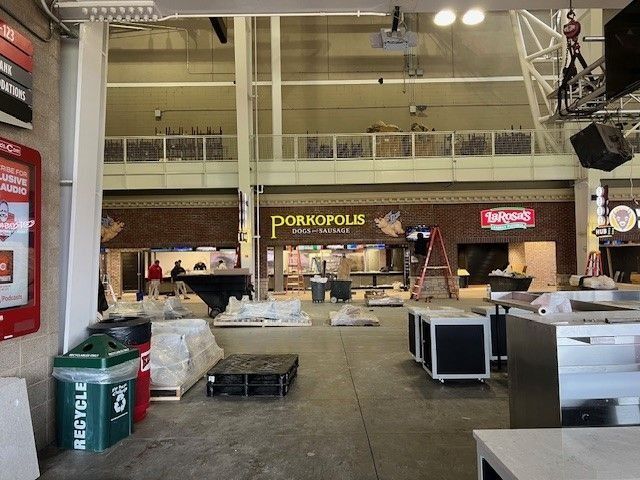 Wide indoor hall with booths, equipment, and tables set up for an event or market