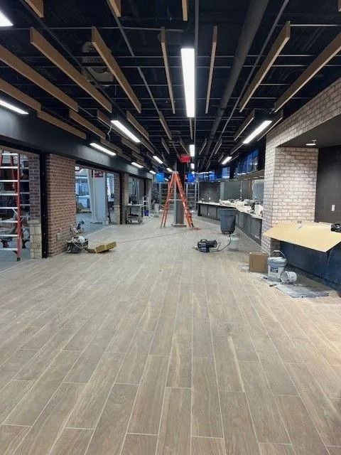 Empty commercial interior under construction with exposed ceiling, wood-look floor, and ladders in the center