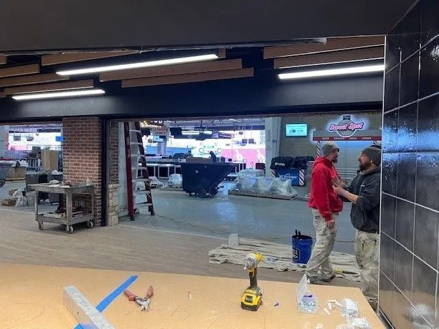 Workers in a large indoor space with tiled walls, tools, and supplies scattered on the floor.