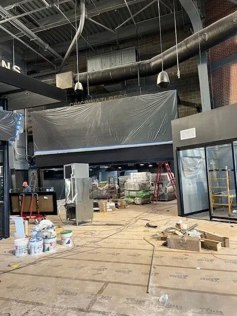 Interior of a store under construction, with exposed ceilings, plastic sheeting, and supplies on a dusty floor.
