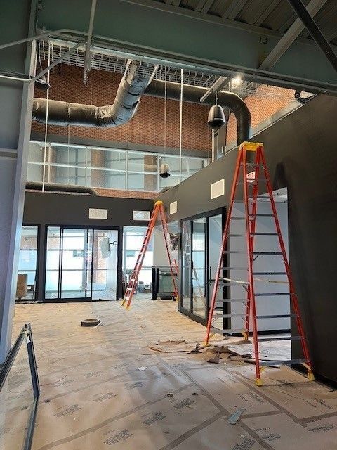 Interior construction site with ladders, exposed ductwork, and unfinished flooring in a commercial space