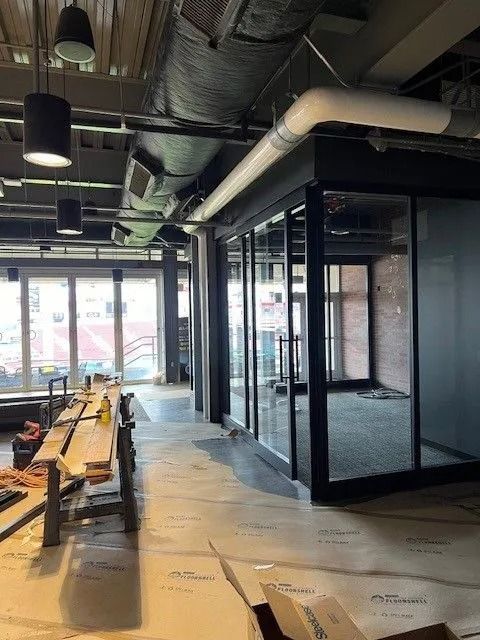 Partially renovated office with glass partitions, exposed ceiling ducts, and construction materials on the floor