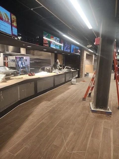 Empty restaurant counter with menu screens, wood floor, and black ceiling lights