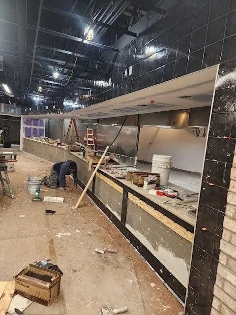 Construction workers installing a long commercial counter in a dimly lit unfinished interior.