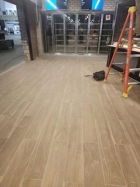 Empty storefront with glass doors, tiled floor, ladder, and cleaning tools near the entrance.