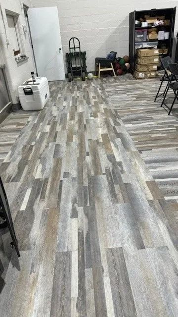 Indoor room with gray wood-look flooring, shelves, and stacked boxes near the back wall