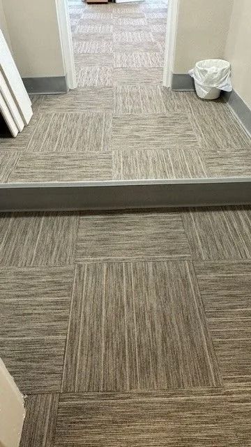 Carpeted hallway with a step up, a doorway ahead, and a trash can on the right.