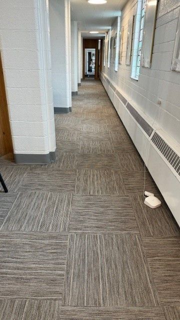 Empty office hallway with white walls, gray carpet, and windows along the right side.