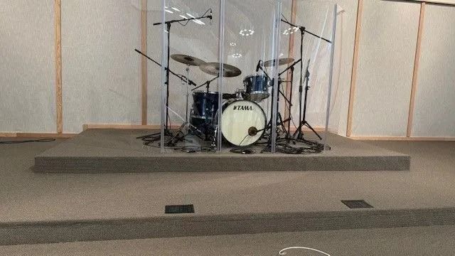 Drum kit on a small stage behind a clear sound shield in a church or auditorium
