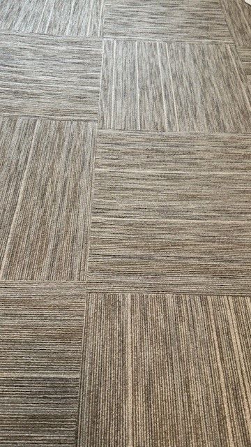 Close-up of beige and gray woven carpet tiles arranged in a staggered pattern